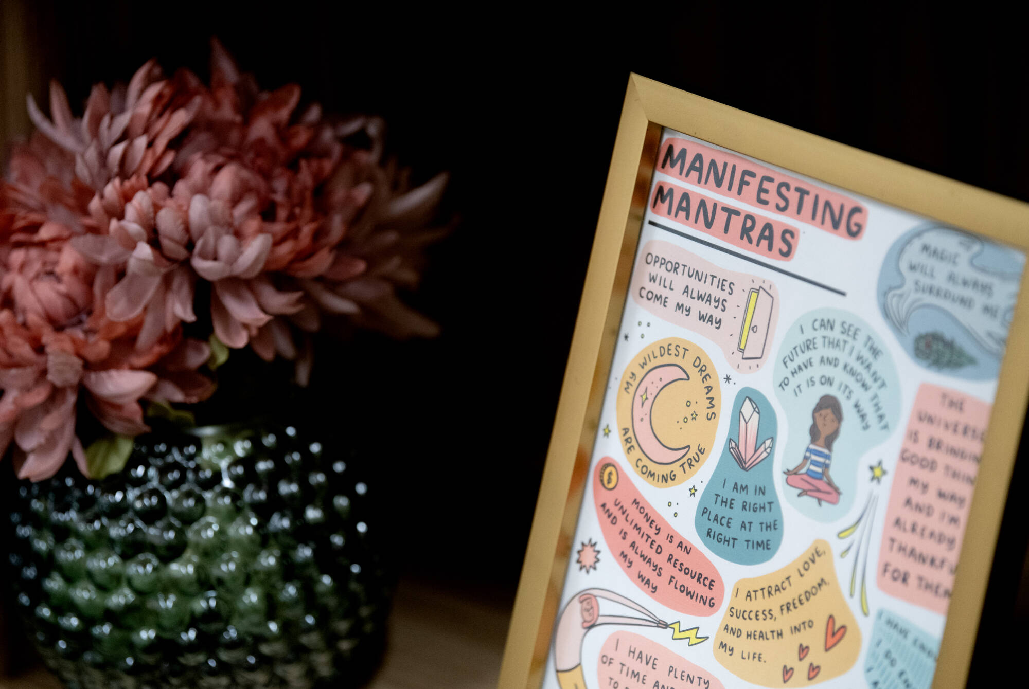 a pink flower in a green, circle vase next to a photo frame with a collage of manifesting mantras
